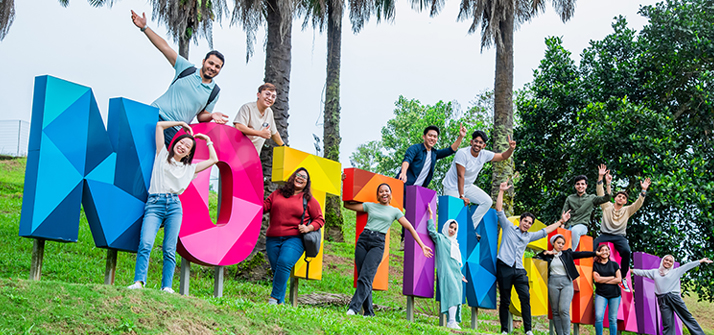 a diverse group of students posing around large, colorful letters that spell out "NOTTINGHAM at the park.